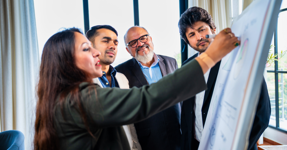 An image of a business woman writing qualitative insights on a board with colleagues looking on.